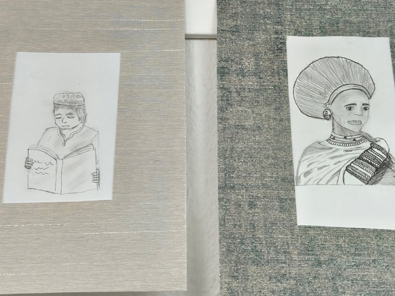 Zwei Zeichnungen auf einem Tisch: Links ein lächelndes Kind mit einem Buch, rechts eine Person in traditioneller Kleidung.