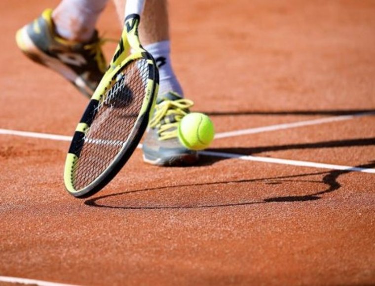 Tennisschläger, Ball, und Füße eines Tennisspielers auf rotem Sand