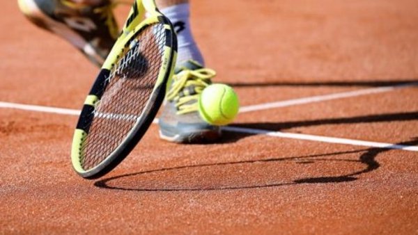 Tennisschläger, Ball, und Füße eines Tennisspielers auf rotem Sand