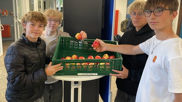 Schüler der Klassenstufe 10 vor der Apfelkiste mit Äpfeln in der Hand.