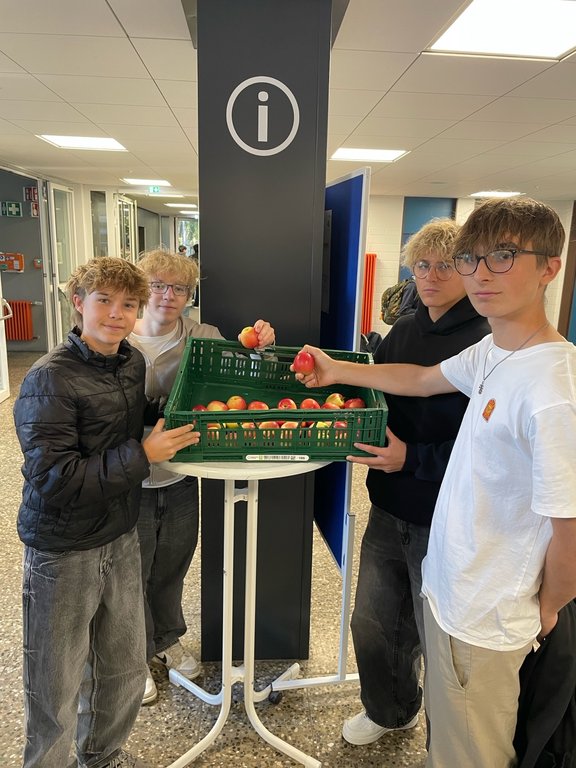 Schüler der Klassenstufe 10 vor der Apfelkiste mit Äpfeln in der Hand.