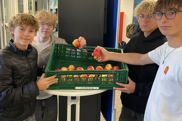 Schüler der Klassenstufe 10 vor der Apfelkiste mit Äpfeln in der Hand.