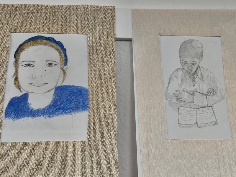 Zwei Porträts in Rahmen; links eine farbige Zeichnung eines Mädchens, rechts eine Bleistiftzeichnung eines Jungen mit Buch.